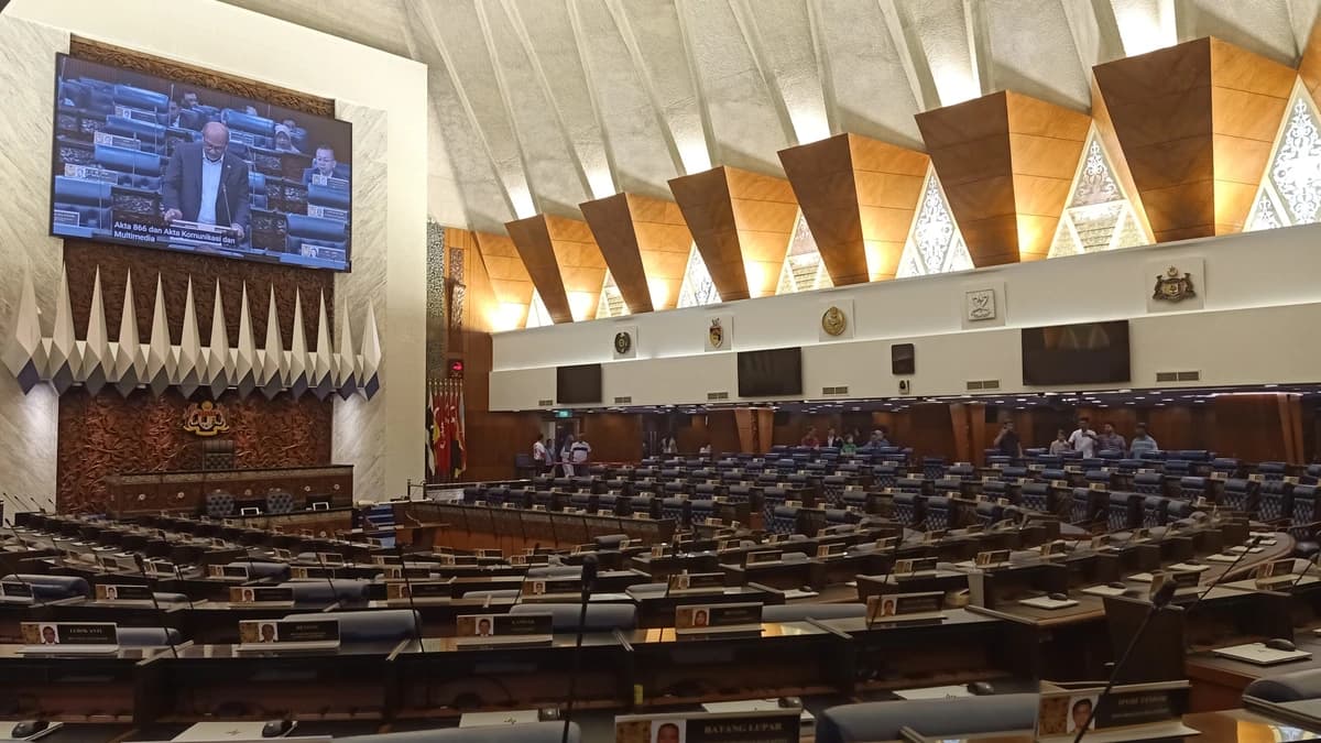 Interior of the Dewan Rakyat chamber in Parliament, with rows of desks and a large screen showing a member speaking