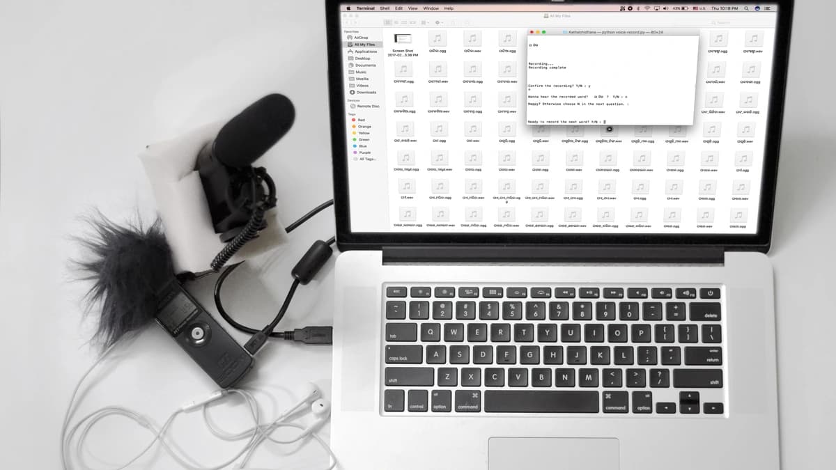 A microphone, a handheld audio recorder and earphones connected to a laptop showing a folder of audio files