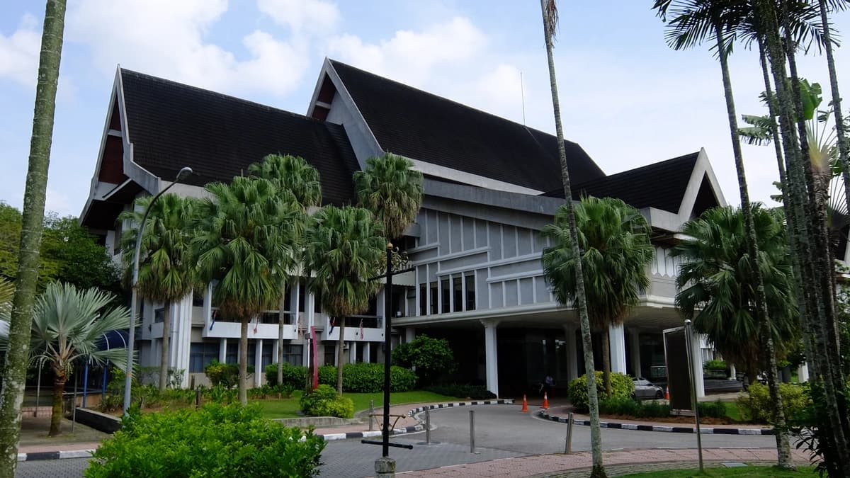 Sultan Ibrahim Chancellor Building at Universiti Teknologi Malaysia, a hall with a dark pitched roof and white columns among palm trees
