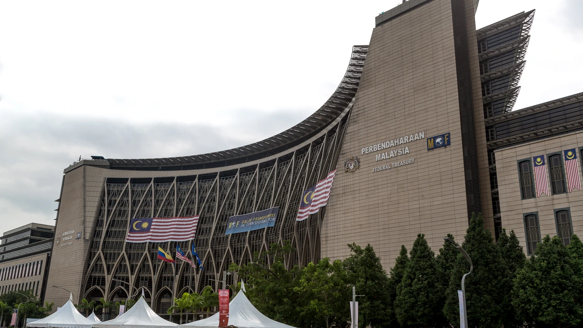 The curved Federal Treasury building in Putrajaya, with the Malaysian flag, a Treasury sign and trees in front