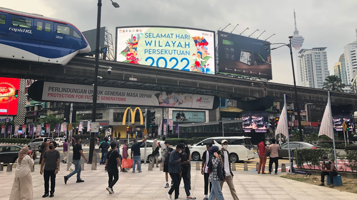 Shoppers and a monorail train at Bukit Bintang in Kuala Lumpur, with digital billboards and the KL Tower behind
