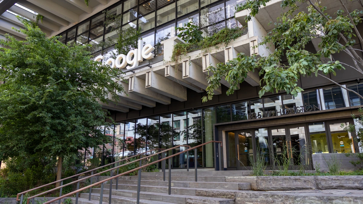 The Google sign on the entrance of Google's New York office at St. John's Terminal, with steps and trees in front of a glass and concrete facade