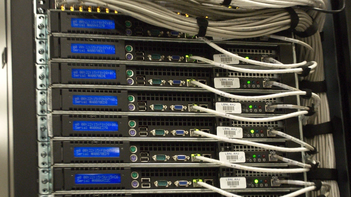 Front of a server rack with rows of black servers, blue status screens and white network cables looped between them