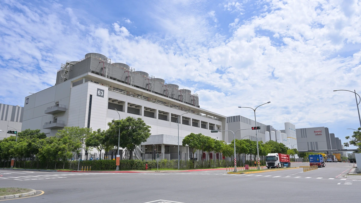 Large white semiconductor factory building with rooftop cooling towers, street trees and the number 63 on its wall