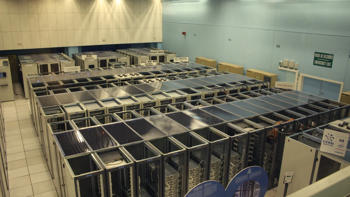 Rows of tall equipment racks in a large data centre hall with a tiled floor and a ceiling of bright light panels