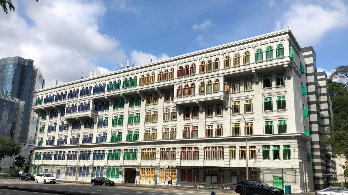 The long white colonial facade of the Old Hill Street Police Station in Singapore, its rows of arched window shutters painted in graduated bands of blue, green, yellow and red, with traffic passing on the road in front