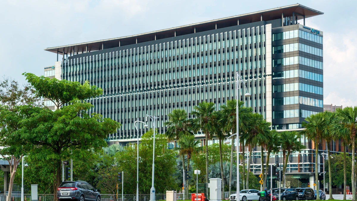 Menara PjH in Putrajaya, a long glass office block with vertical metal fins, seen across a landscaped forecourt of palms and young trees with cars parked at the roadside