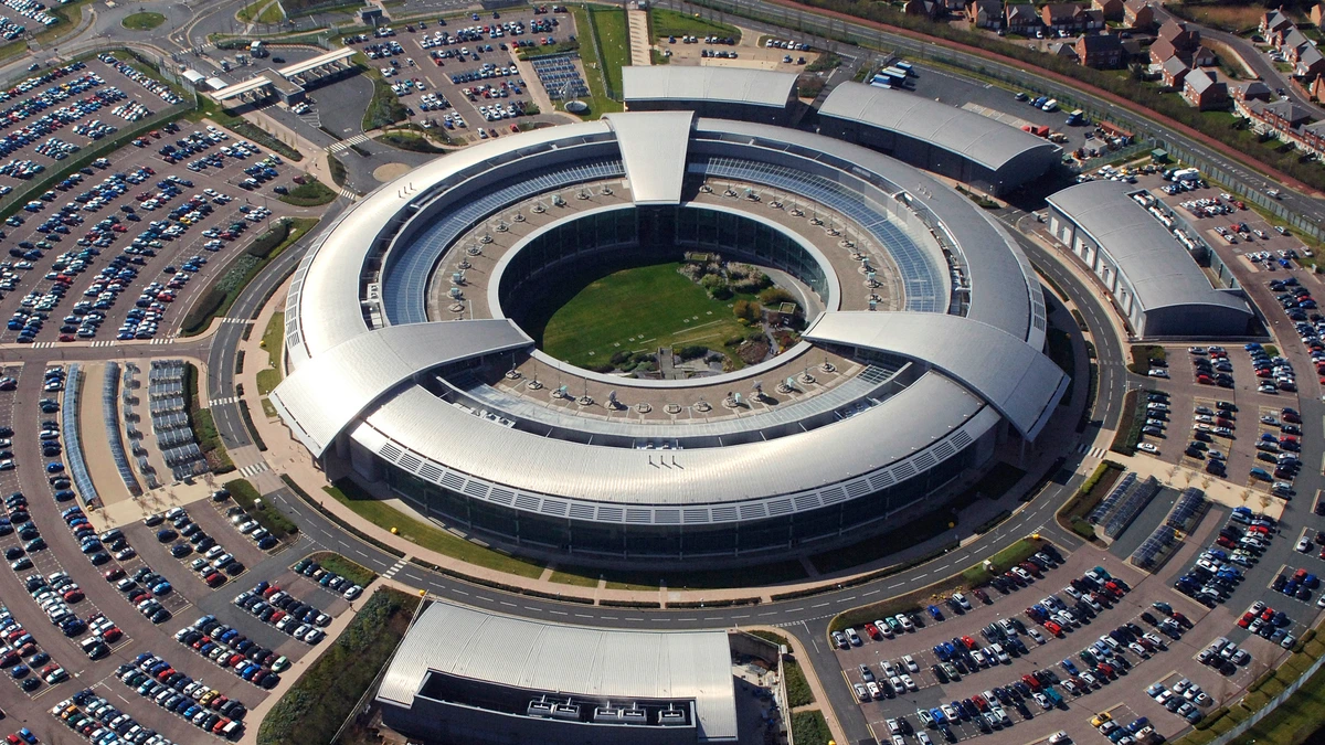 Aerial view of a large ring-shaped office building with solar panels, surrounded by car parks and fields