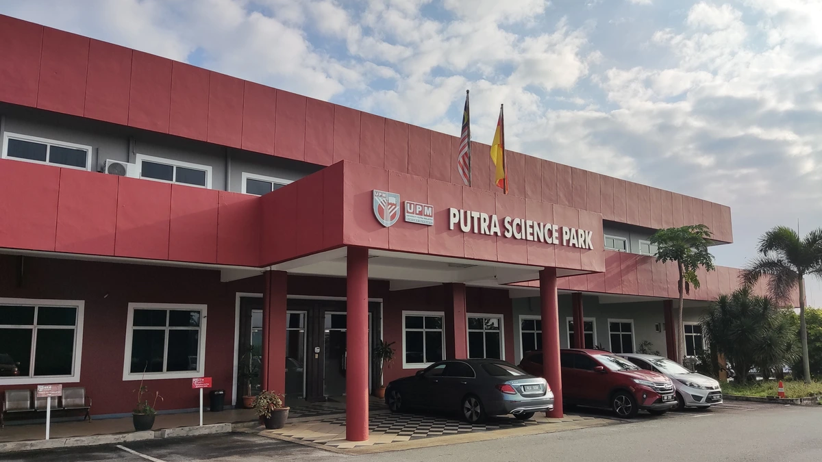 Red two-storey Putra Science Park building at UPM with its name above the entrance, two flags and cars parked in front