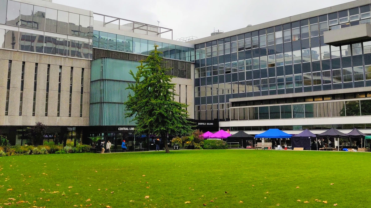 The Central Library and Sherfield Building of Imperial College London around a green lawn with a tree and market stalls