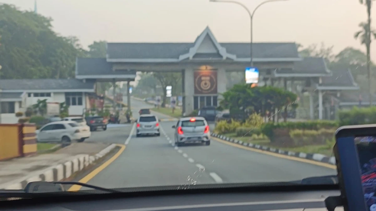 A campus entrance gateway with a covered roof structure at the end of a road, seen through a car windscreen on a hazy day